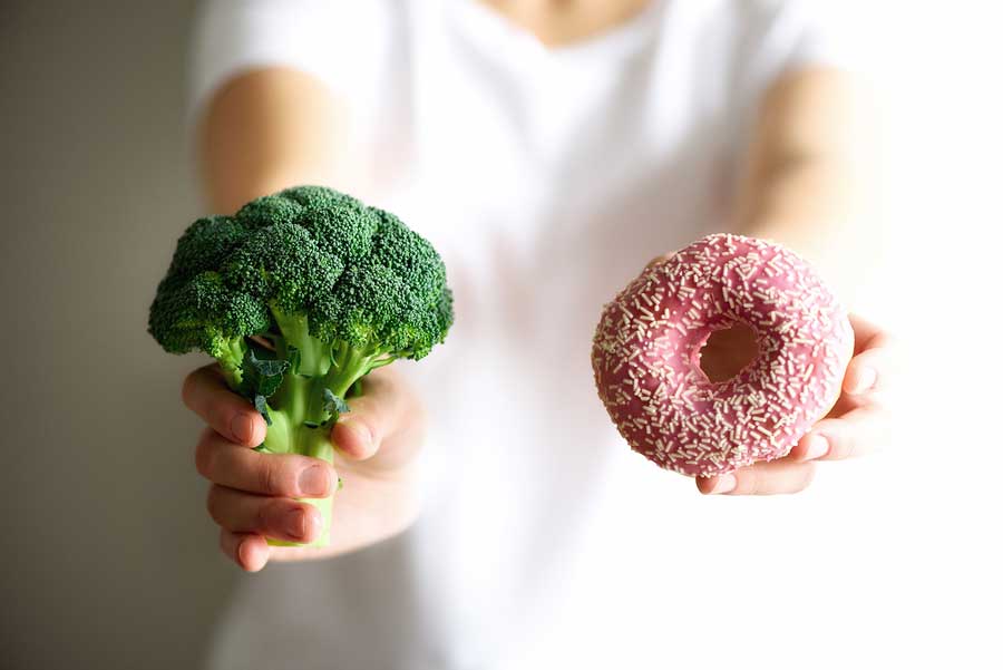 Closeup of a hand holding a head of broccoli and the other hand holding a donut