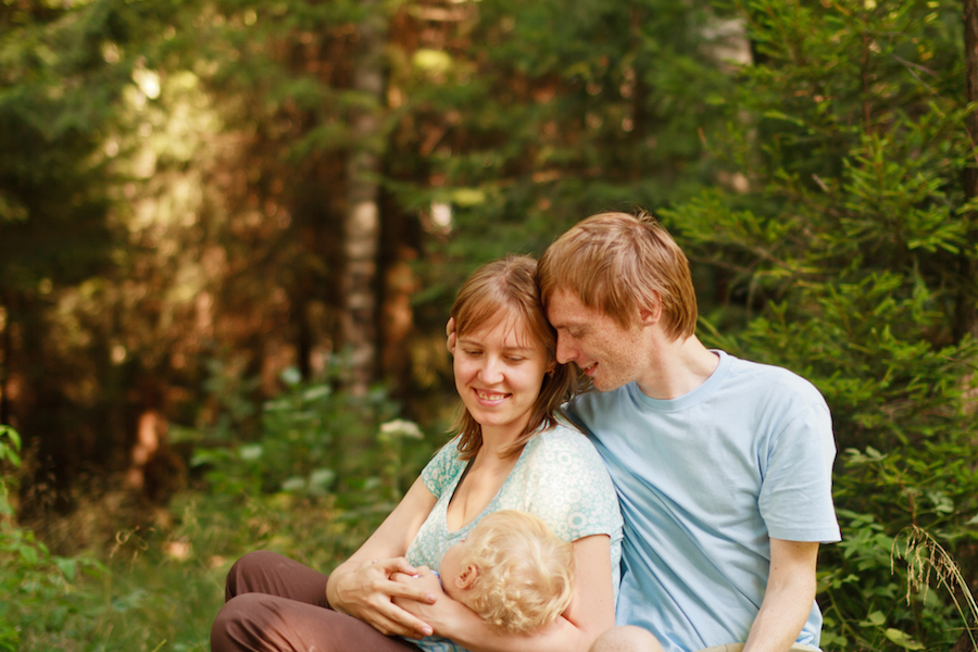 A young couple sitting outdoors holding their baby