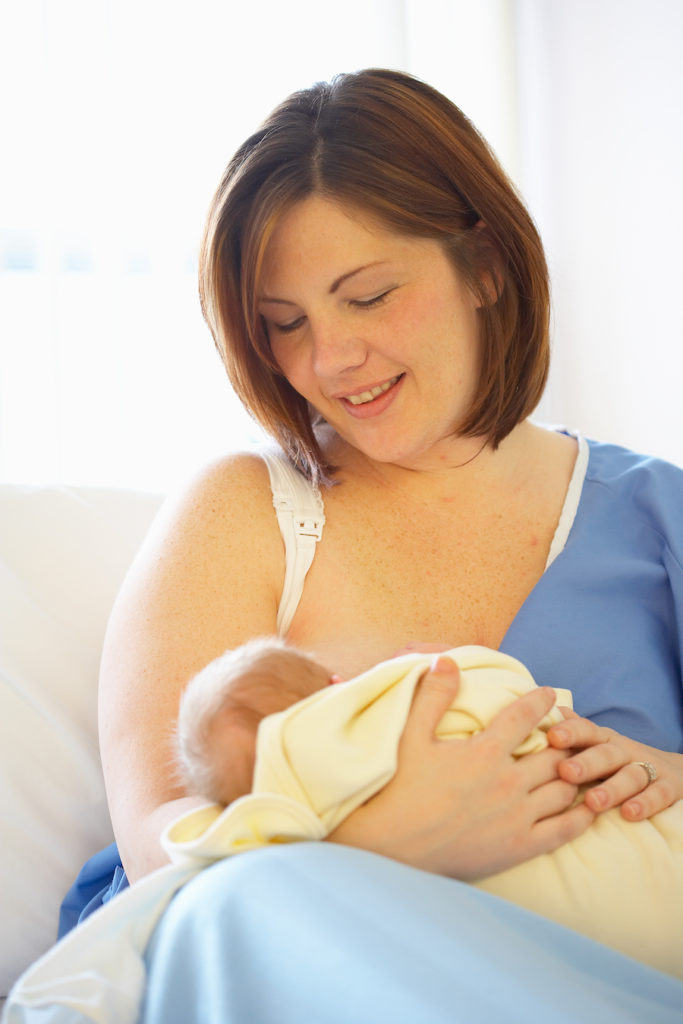 A mother sitting up in a hospital gown breastfeeding her newborn
