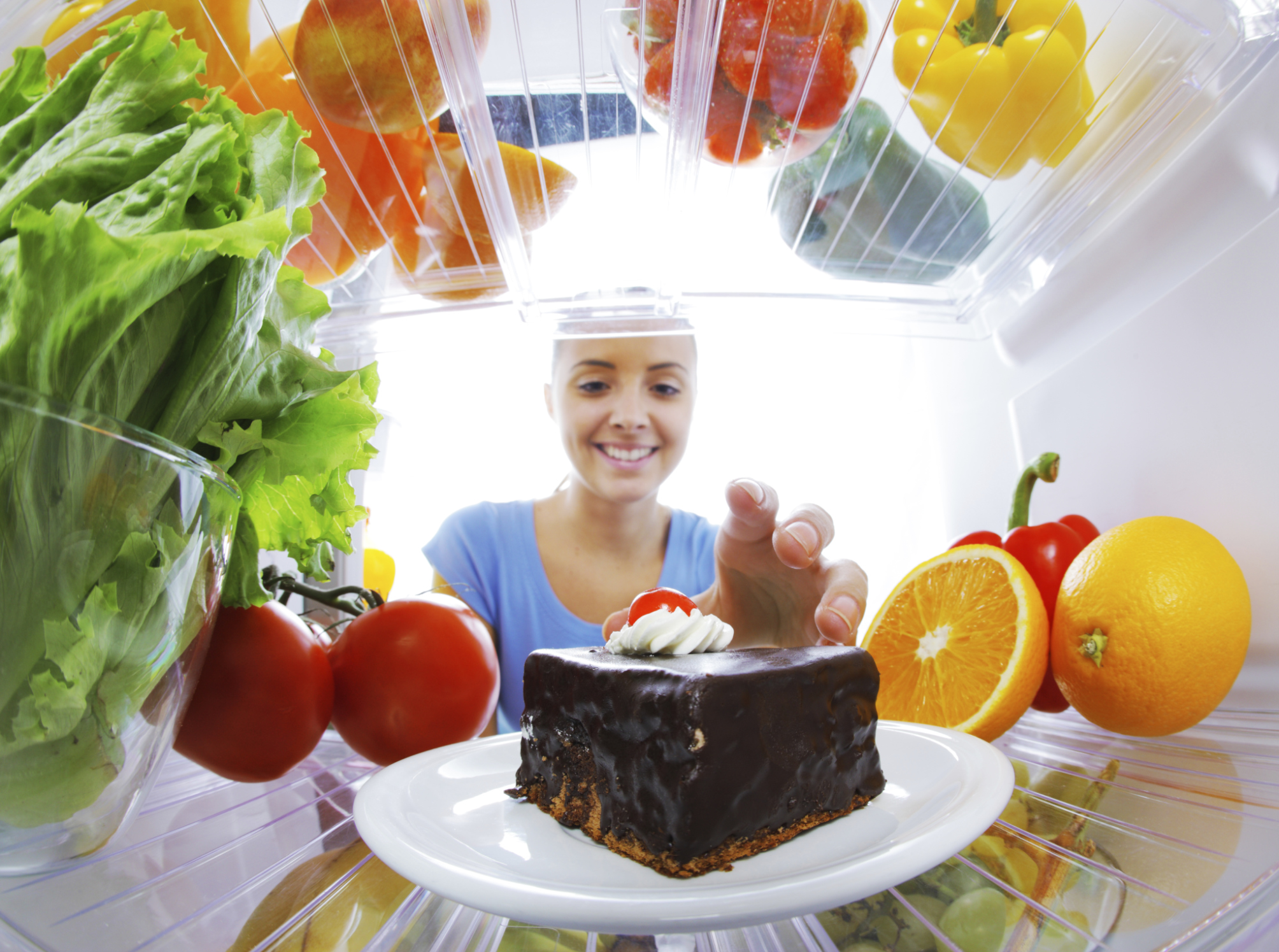 A woman smiling while reaching for a piece of chocolate cake in a fridge