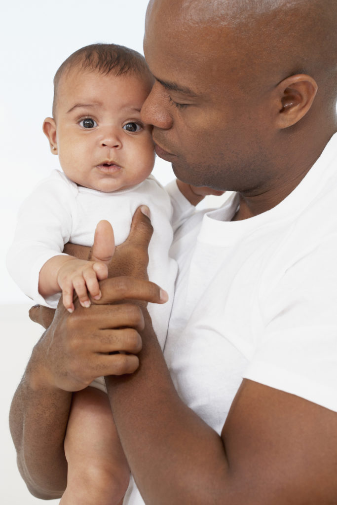 An African American man holding his baby to his chest