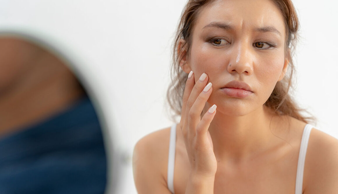 Closeup of a Young Woman Concerningly Looking at Her Face in a Mirror Experiencing the Effects of PCOS