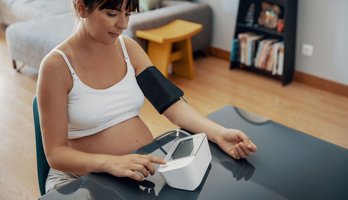 A Pregnant Woman Sitting Down Wearing A Blood Pressure Cuff Checking Her Blood Pressure What Is Preeclampsia