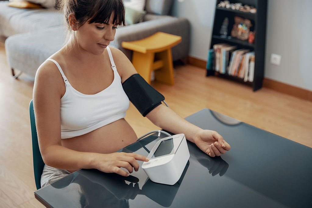 A Pregnant Woman Sitting Down Wearing A Blood Pressure Cuff Checking Her Blood Pressure What Is Preeclampsia